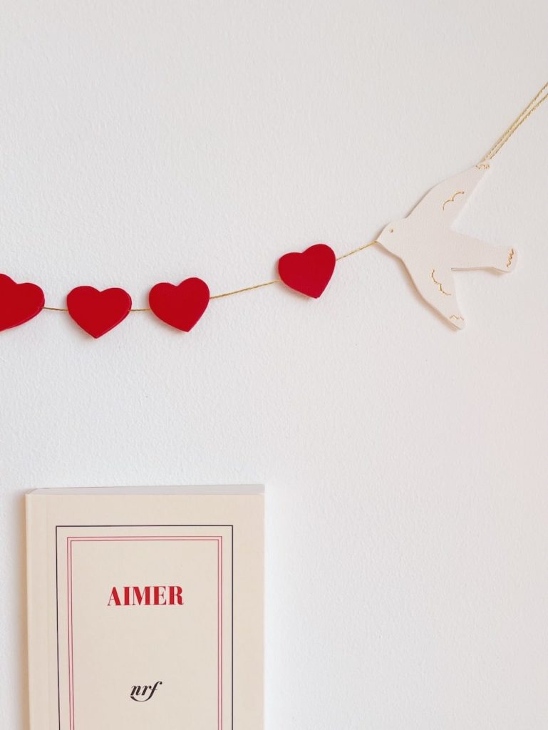 Ribambelle "de l'amour dans l'air". Guirlande décorative pensée comme un bijou mural avec oiseaux blancs aux détails dorés à chaud à l'or véritable et coeurs rouges, roses, poudre, nude, or clair ou or rose selon les modèles. Décoration murale poétique pour l'intérieur. Cet objet décoratif unique permet de sublimer avec élégance et raffinement n'importe quelle pièce de la maison et fait aussi un joli cadeau original de Saint-Valentin, fête des mères, pour un baptême, des fiançailles ou un mariage. Artisanat d'art, façonnage en cuir surcyclé ( excédents de tanneries françaises ennoblis) sur la côte d'Opale, Hauts-de-France