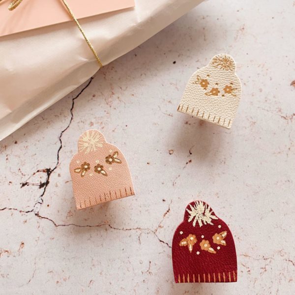Broche en cuir en forme de bonnet d'hiver avec motif floral doré, en coloris ivoire, bordeaux et rose poudré.