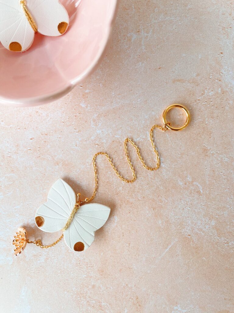 Suspension poétique papillon en cuir fait main, bijou d’intérieur avec fleur de cerisier et quartz rose, à suspendre sous une étagère ou un luminaire.